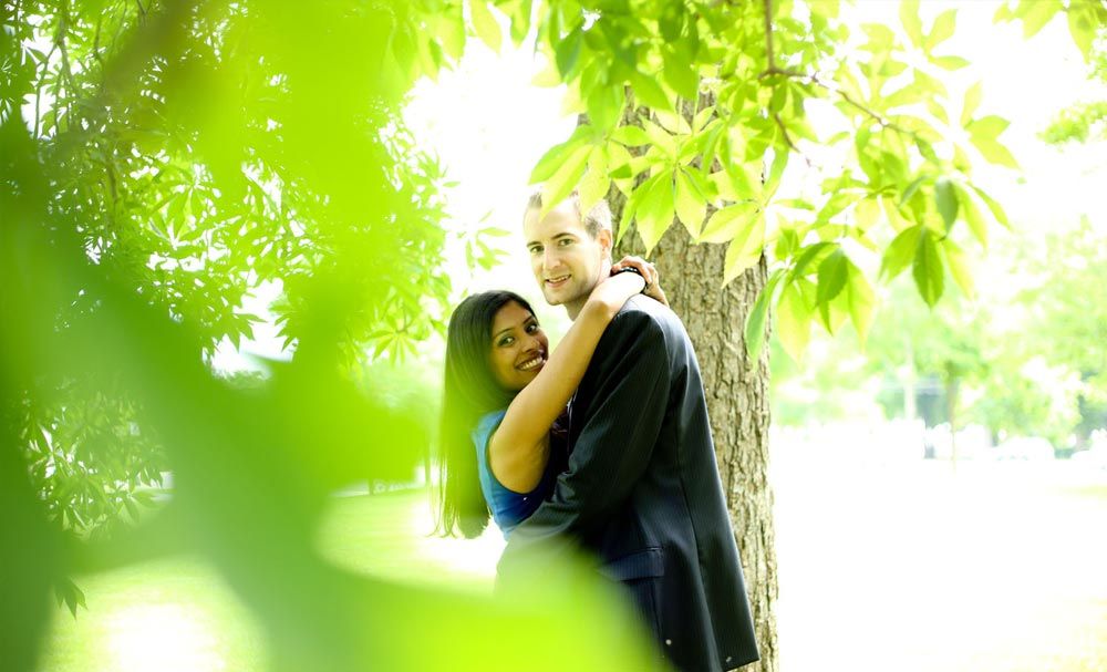 Couple posing together beneath leafy trees