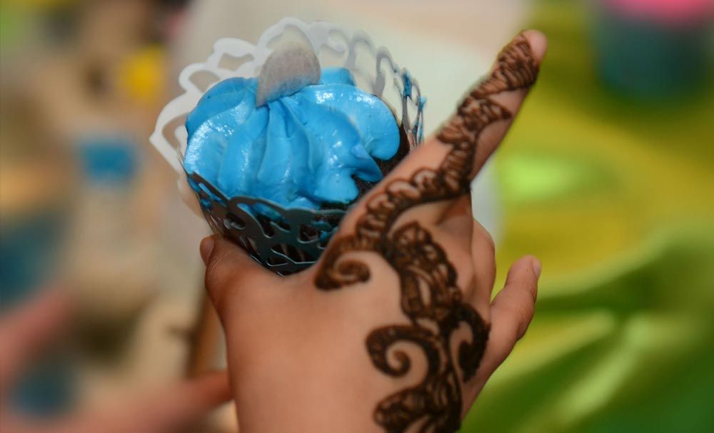 Hennaed hand holding a blue decorative cupcake