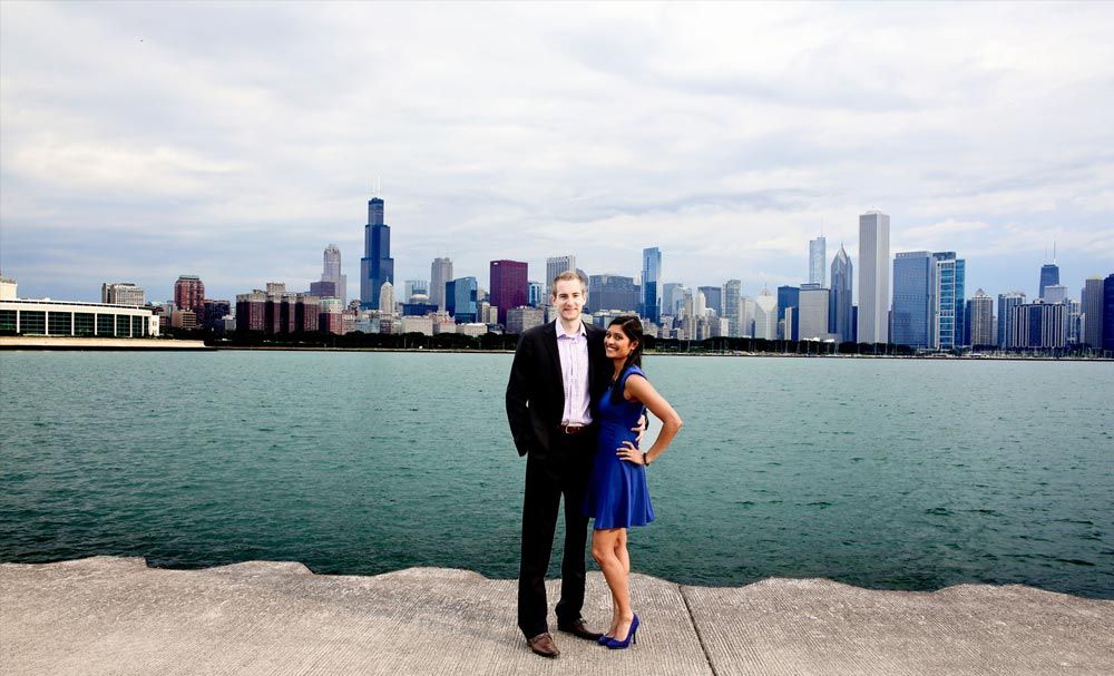 Couple posing beside the water with a city skyline